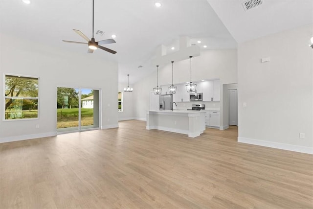 unfurnished living room with sink, light wood-type flooring, ceiling fan with notable chandelier, and high vaulted ceiling