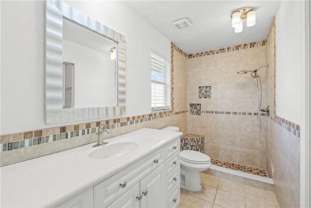 bathroom featuring tile patterned flooring, a tile shower, vanity, toilet, and tile walls