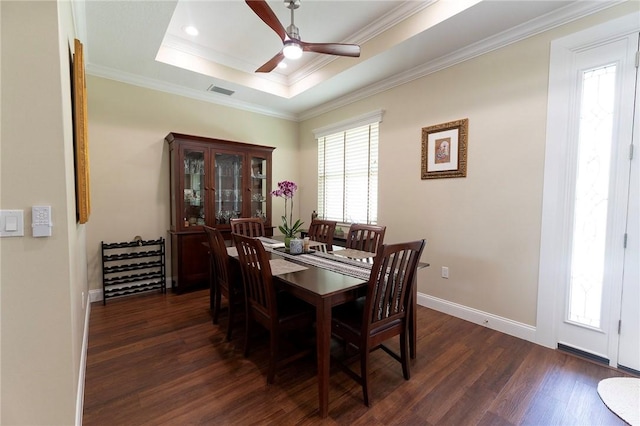 dining area featuring dark wood finished floors, a ceiling fan, a raised ceiling, crown molding, and baseboards