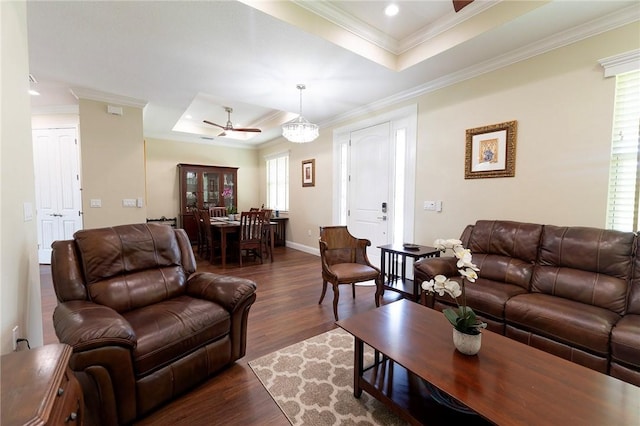 living area featuring a raised ceiling, ceiling fan, dark wood-type flooring, ornamental molding, and baseboards
