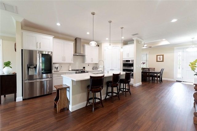 kitchen with appliances with stainless steel finishes, wall chimney range hood, dark wood finished floors, ornamental molding, and light countertops