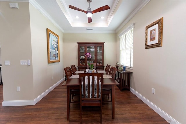 dining space with ceiling fan, a raised ceiling, dark wood finished floors, baseboards, and ornamental molding