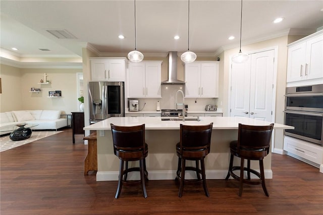 kitchen featuring wall chimney exhaust hood, appliances with stainless steel finishes, a sink, light countertops, and an island with sink
