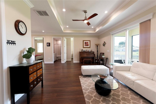 living area with dark wood finished floors, a ceiling fan, baseboards, crown molding, and a tray ceiling