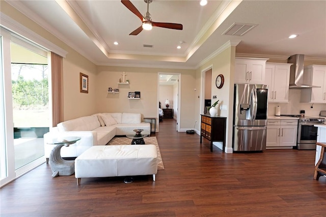 living room with a tray ceiling, ceiling fan, dark wood-style flooring, crown molding, and recessed lighting
