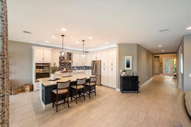 11706 SW Brighton Falls Dr, Port St Lucie, FL 34987 - kitchen with appliances with stainless steel finishes, wall chimney exhaust hood, decorative backsplash, an island with sink, and a breakfast bar area