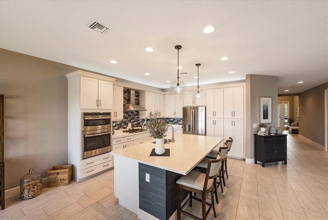 11706 SW Brighton Falls Dr, Port St Lucie, FL 34987 - kitchen with stainless steel appliances, wall chimney exhaust hood, tasteful backsplash, a breakfast bar, and recessed lighting