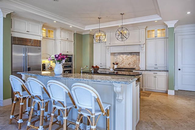 kitchen with dark stone counters, pendant lighting, backsplash, and a center island with sink