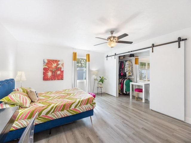 bedroom featuring ceiling fan, a barn door, light hardwood / wood-style flooring, and a closet