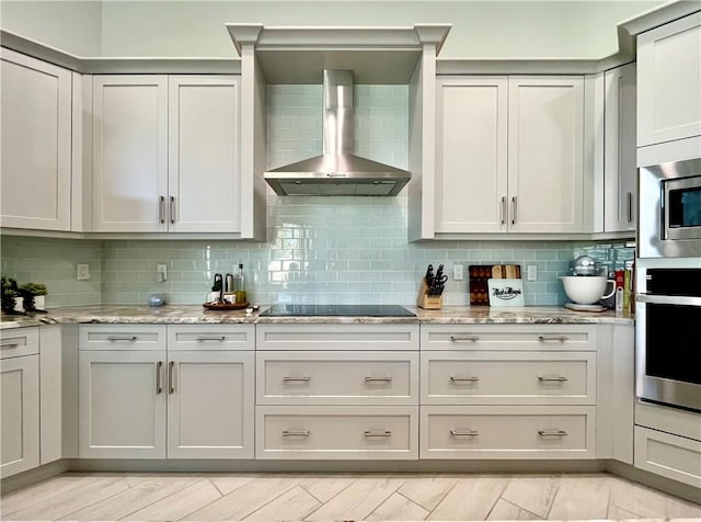 kitchen with appliances with stainless steel finishes, decorative backsplash, light stone counters, and wall chimney exhaust hood