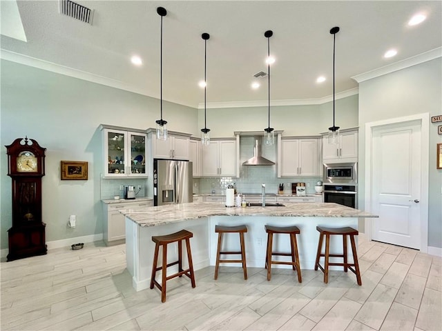 kitchen with pendant lighting, stainless steel appliances, a large island with sink, and wall chimney range hood