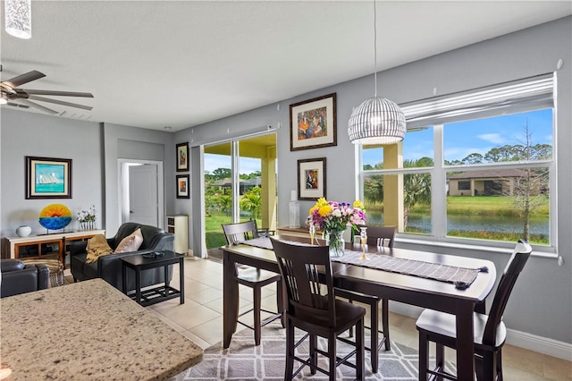 dining space featuring a water view, light tile patterned floors, baseboards, and a ceiling fan