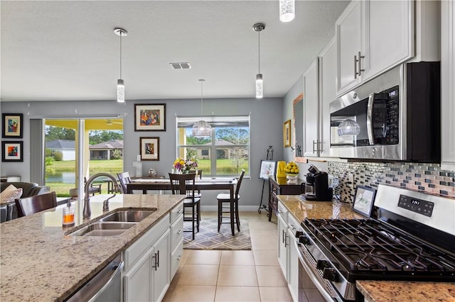 kitchen with light tile patterned floors, backsplash, appliances with stainless steel finishes, a sink, and light stone countertops