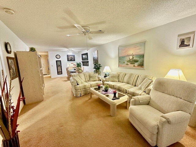 living room featuring a textured ceiling, light colored carpet, and ceiling fan