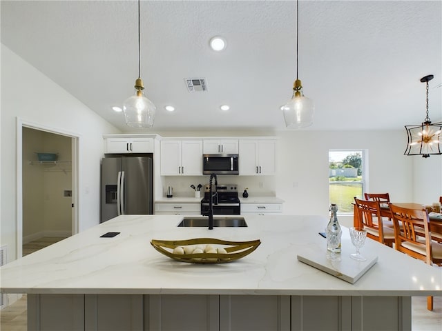 kitchen with a large island with sink, hanging light fixtures, and stainless steel appliances