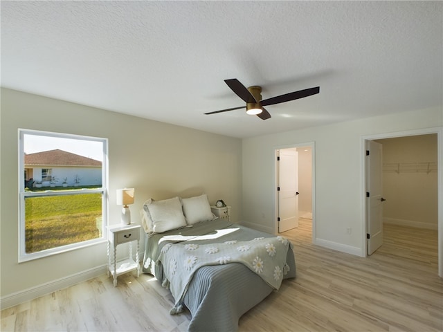 bedroom with ceiling fan, light hardwood / wood-style flooring, a textured ceiling, a walk in closet, and a closet