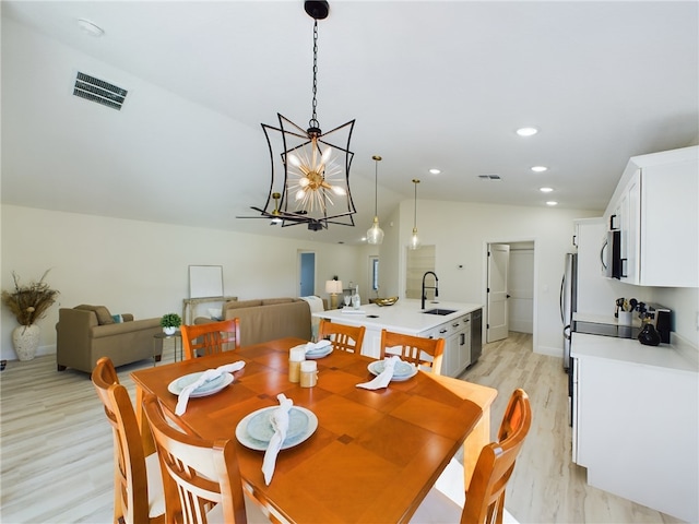 dining space with a chandelier, light wood-type flooring, vaulted ceiling, and sink