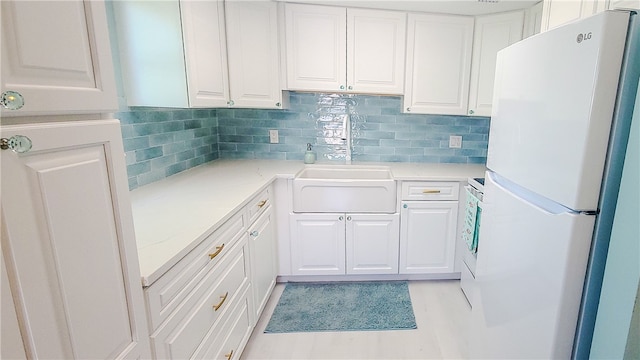 kitchen featuring tasteful backsplash, white cabinetry, white refrigerator, and sink