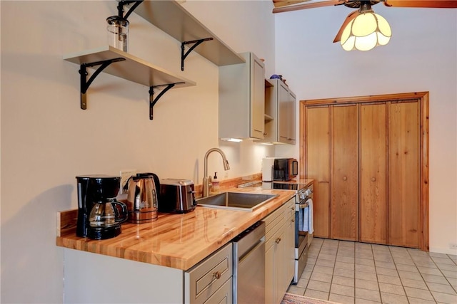 kitchen with light tile patterned floors, stainless steel appliances, wood counters, a sink, and a ceiling fan