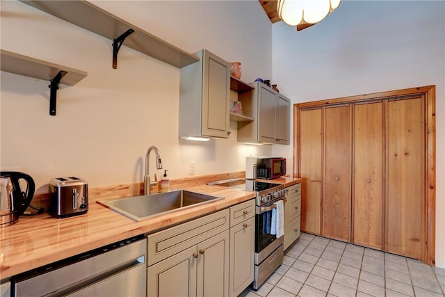 kitchen featuring light tile patterned floors, butcher block counters, a sink, appliances with stainless steel finishes, and open shelves