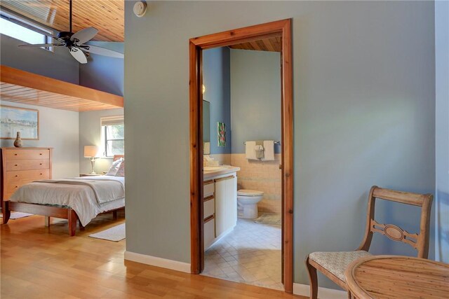 bedroom featuring wooden ceiling, connected bathroom, wood finished floors, tile walls, and wainscoting