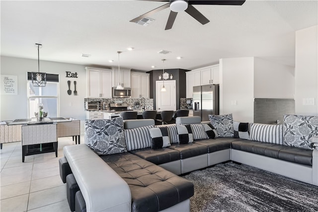 tiled living room with ceiling fan with notable chandelier