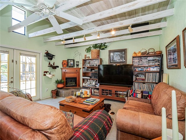 living area with a fireplace with raised hearth, ceiling fan, beam ceiling, french doors, and rail lighting