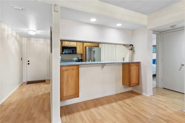 25 Plantation Dr Unit 201, Vero Beach, FL 32966 - kitchen with black microwave, freestanding refrigerator, light wood finished floors, brown cabinetry, and light stone counters