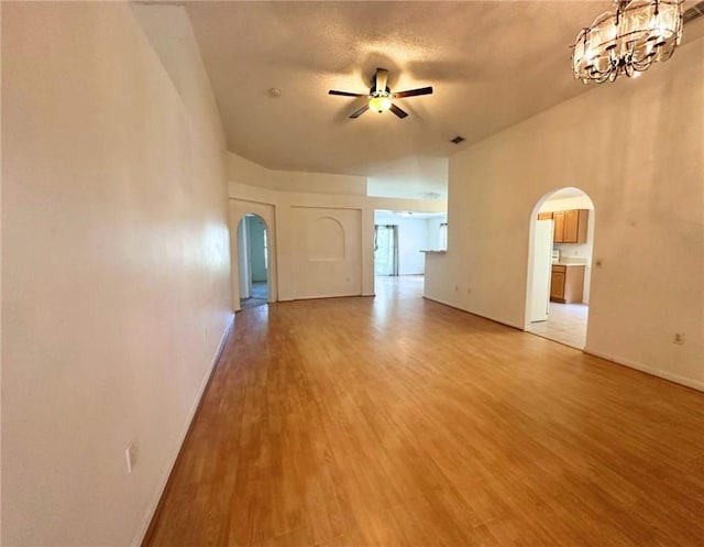 unfurnished living room featuring arched walkways, a ceiling fan, light wood-style floors, baseboards, and a chandelier