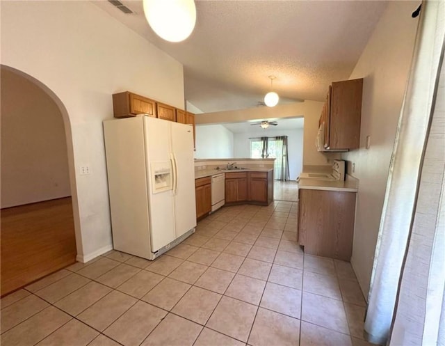 kitchen featuring white appliances, vaulted ceiling, light tile patterned floors, a peninsula, and a sink