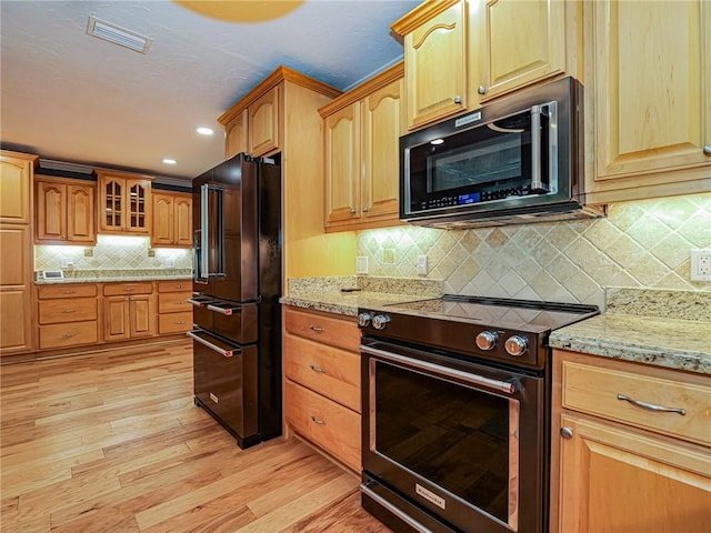 kitchen with stainless steel electric range, light wood-style flooring, light stone countertops, visible vents, and high end black refrigerator