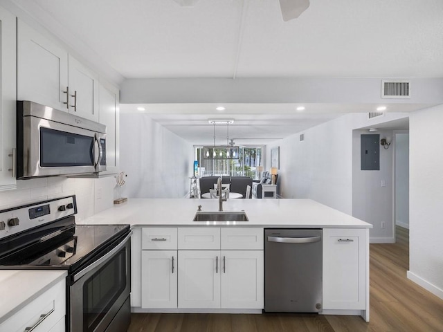 kitchen featuring a sink, a peninsula, wood finished floors, white cabinets, and appliances with stainless steel finishes