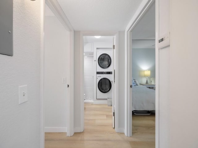 clothes washing area featuring baseboards, laundry area, stacked washing maching and dryer, and light wood-style flooring