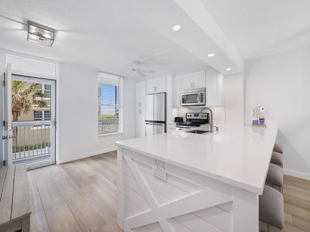 kitchen with a breakfast bar area, appliances with stainless steel finishes, light wood-type flooring, baseboards, and a peninsula