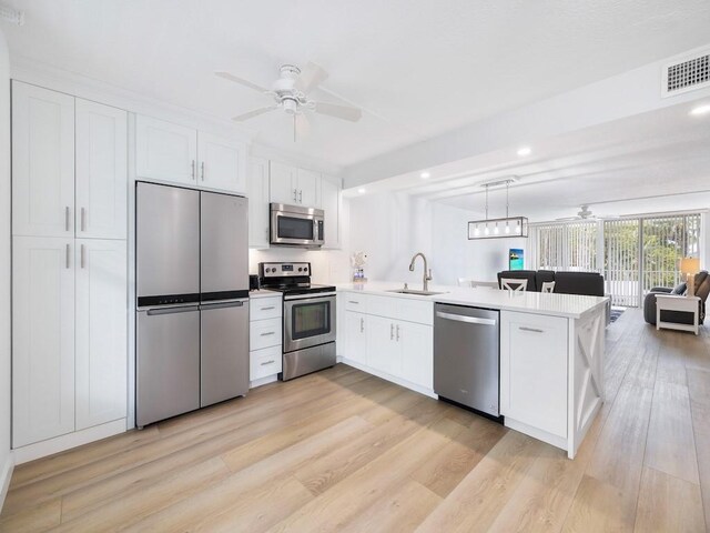 kitchen with a sink, stainless steel appliances, open floor plan, a ceiling fan, and a peninsula