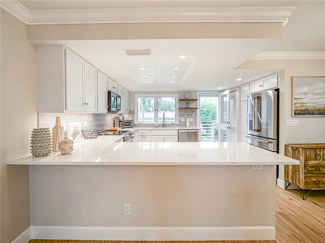 kitchen featuring stainless steel appliances, decorative backsplash, light hardwood / wood-style floors, white cabinets, and kitchen peninsula