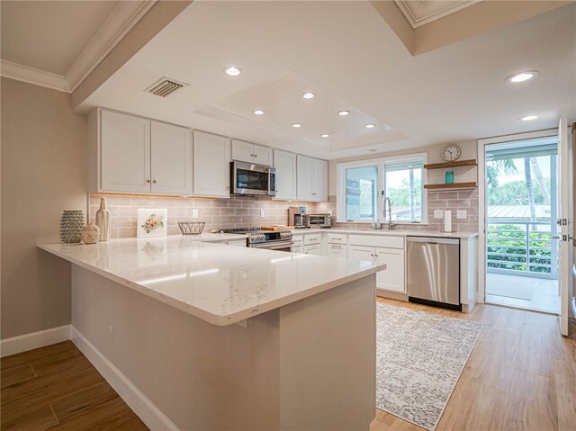 kitchen with stainless steel appliances, kitchen peninsula, tasteful backsplash, white cabinetry, and light hardwood / wood-style flooring