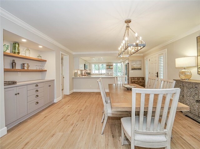 dining area with light wood-type flooring, an inviting chandelier, and ornamental molding