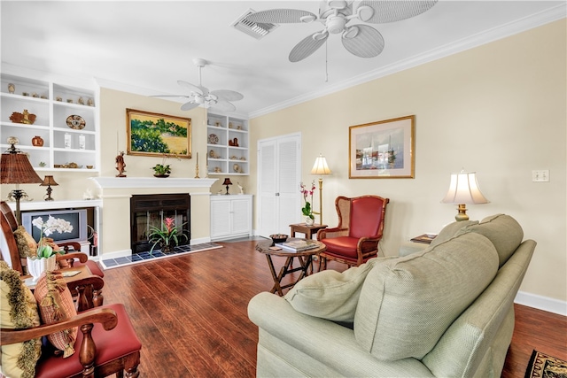 living room with ceiling fan, built in features, dark hardwood / wood-style flooring, and ornamental molding