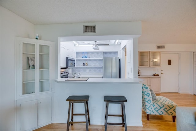 1845 Robalo Dr Unit 101D, Vero Beach, FL 32960 - kitchen with appliances with stainless steel finishes, light wood-style flooring, a breakfast bar area, a peninsula, and open shelves