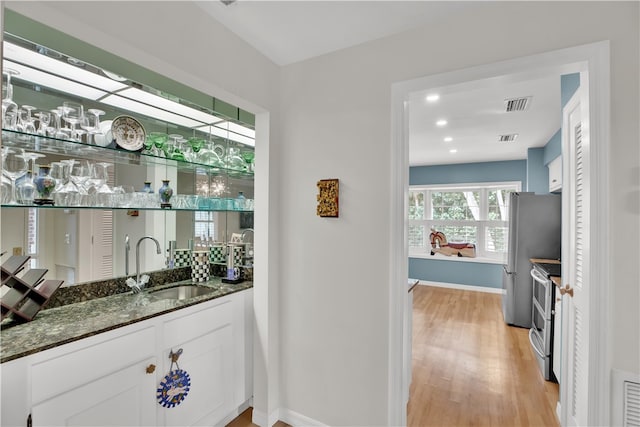 bar featuring sink, stainless steel appliances, dark stone counters, white cabinets, and light wood-type flooring