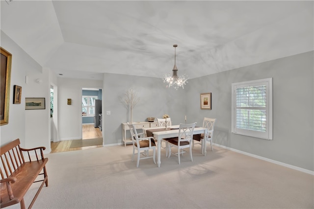 dining room featuring lofted ceiling, a healthy amount of sunlight, light colored carpet, and an inviting chandelier