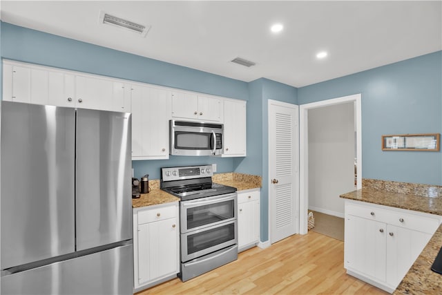 kitchen with light stone countertops, appliances with stainless steel finishes, white cabinetry, and light hardwood / wood-style flooring