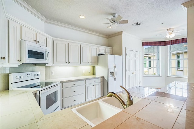 kitchen featuring white appliances, a textured ceiling, white cabinets, and tile counters