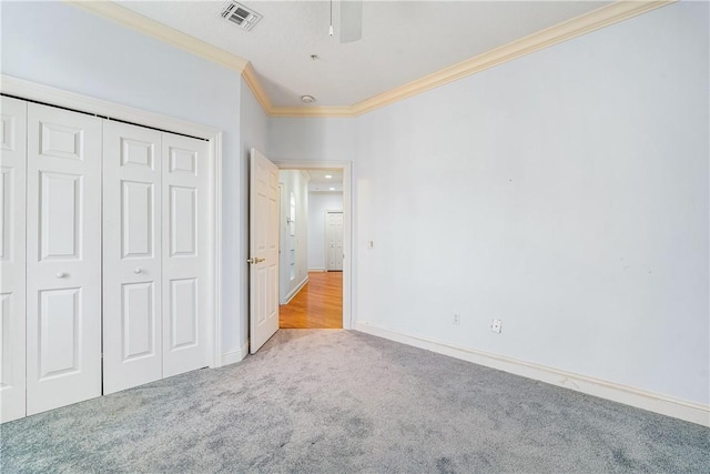 unfurnished bedroom featuring ceiling fan, light colored carpet, a closet, and crown molding