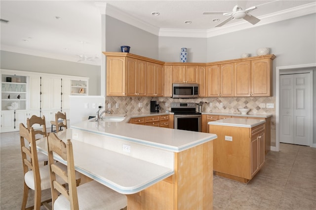 kitchen with sink, a breakfast bar area, ornamental molding, appliances with stainless steel finishes, and kitchen peninsula