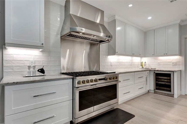 kitchen featuring beverage cooler, light stone countertops, range with two ovens, white cabinets, and wall chimney exhaust hood