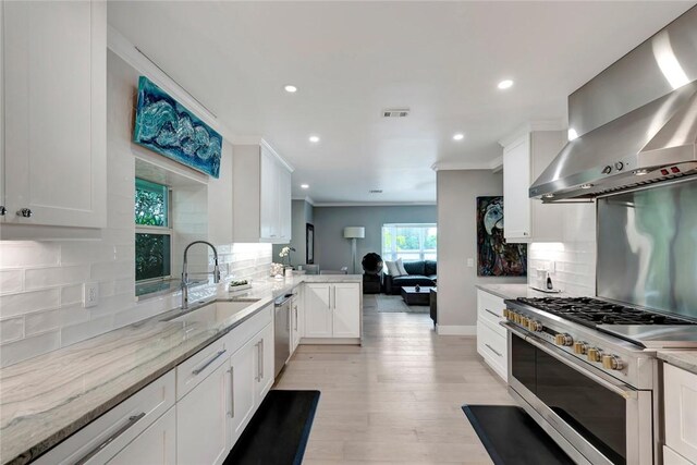 kitchen featuring visible vents, ornamental molding, a sink, appliances with stainless steel finishes, and wall chimney range hood