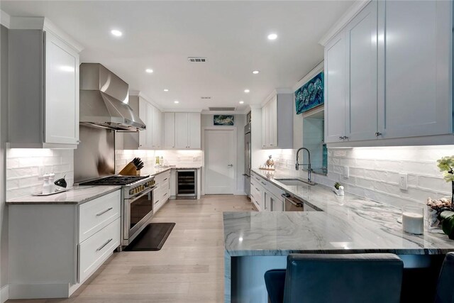 kitchen with visible vents, beverage cooler, a sink, wall chimney range hood, and high end range