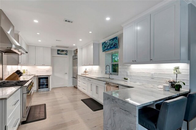 kitchen featuring ventilation hood, light stone countertops, wine cooler, high end appliances, and a sink